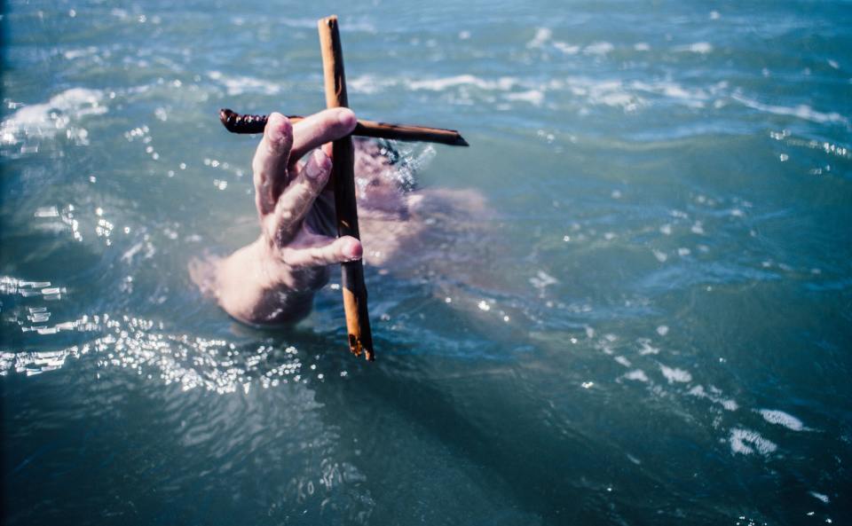 Photo by Tim Marshall on Unsplash; Man holding a cross in the sea